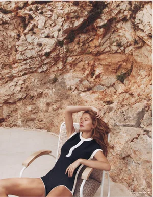 Model relaxing in a white chair wearing a dark swimsuit against a rocky cliff face