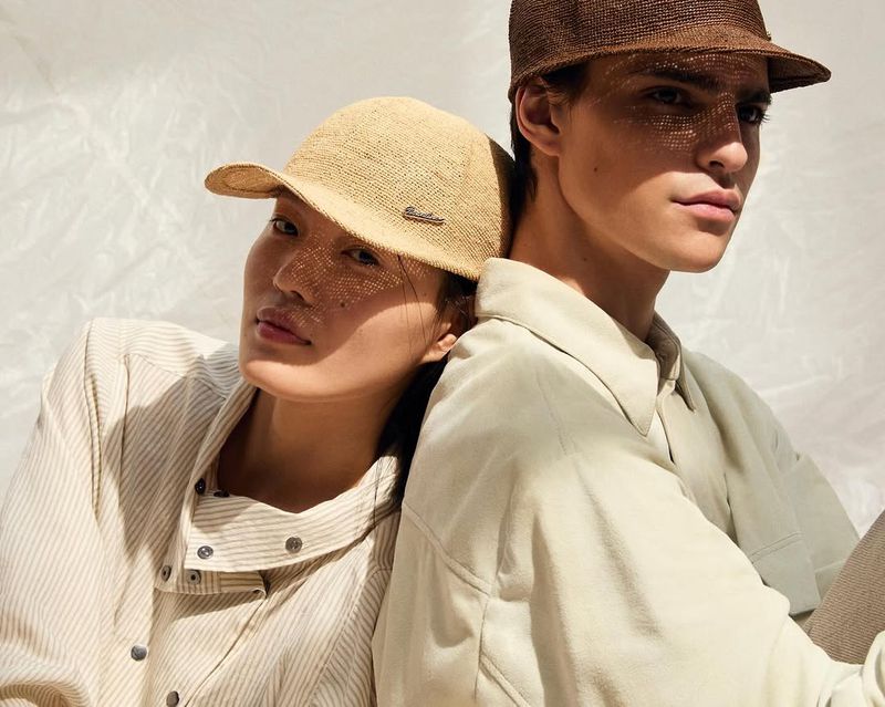 Two models leaning back-to-back wearing woven caps and light shirts against a white background for Borsalino