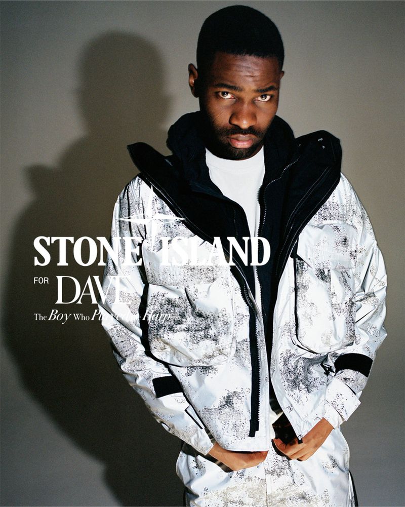 Man wearing a white and black patterned jacket and black hoodie against a plain grey studio background with bold text overlays.