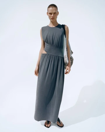 Model wearing a grey sleeveless maxi dress with side cutouts against a white seamless background