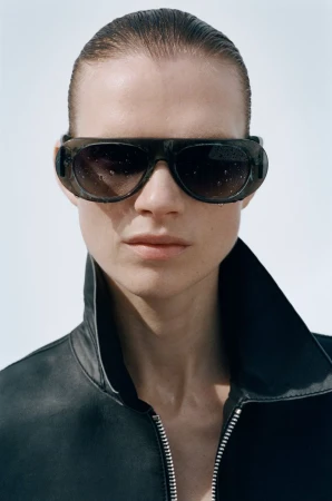 Close-up portrait of a model wearing dark sunglasses and a black leather jacket against a light background