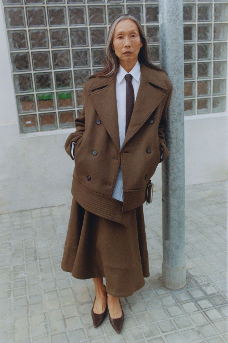 Model Yuri Fukuhara wearing a brown wool coat and skirt leaning against a pole for Puss Puss Magazine editorial.