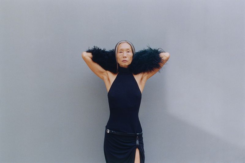 Model Yuri Fukuhara in black halter dress with fur stole against a grey background for Puss Puss Magazine