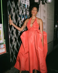Woman in a vibrant red halter dress posing in front of a metal security gate at night