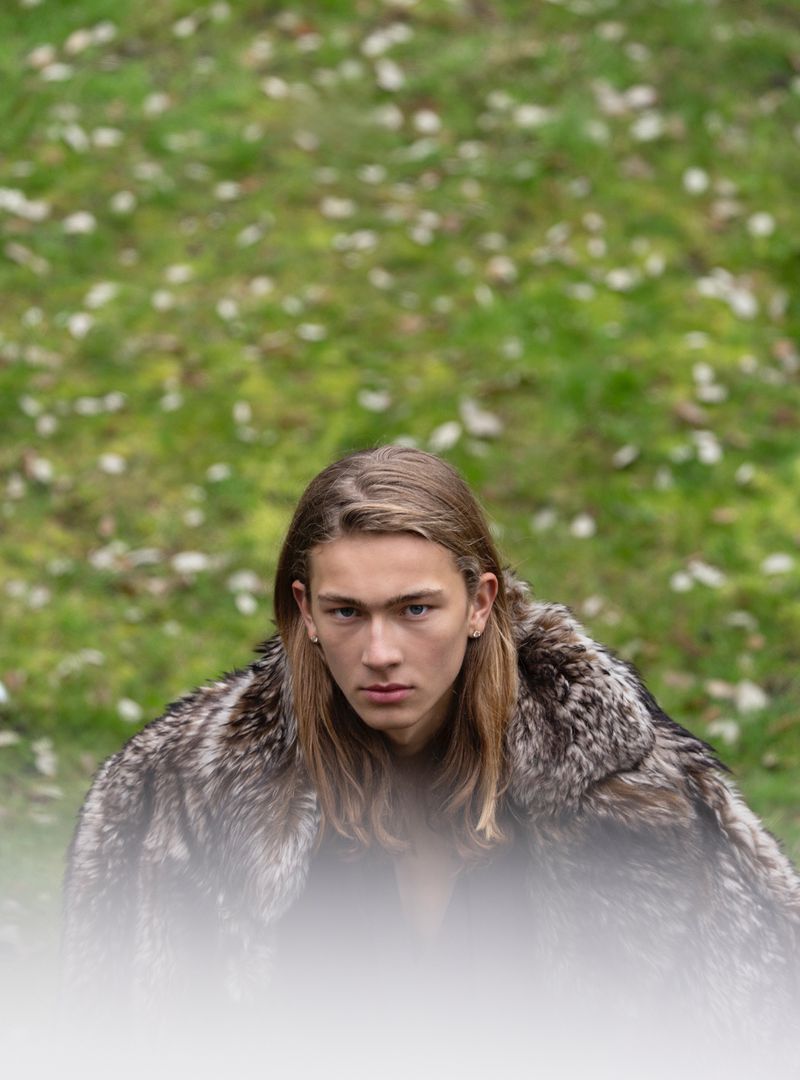 Model with long blonde hair wearing a textured faux fur coat outdoors against a green grass background.