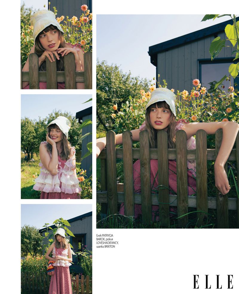 Model wearing a white bucket hat and ruffled top leaning on a wooden fence in a garden for Elle Bulgaria magazine editorial