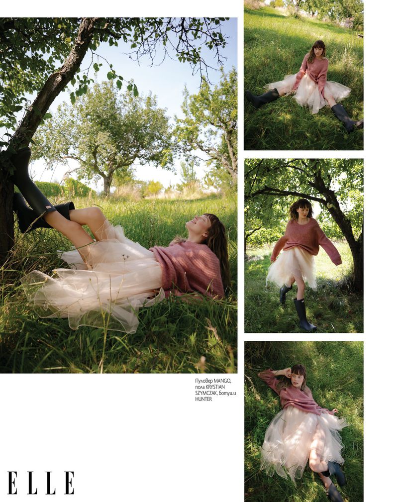 Model in a pink sweater and tulle skirt lying on green grass outdoors in an orchard for Elle Bulgaria