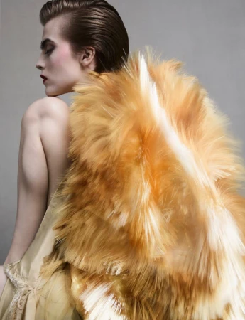 Model in profile wearing a textured orange feathered garment against a plain grey backdrop