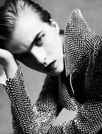 Close-up monochrome portrait of a model with dark lipstick wearing a patterned textured high-collar jacket.