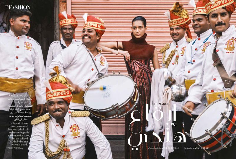 Model in a brown sleeveless turtleneck top posing amid a brass band in uniform on a street for Harper's Bazaar Arabia