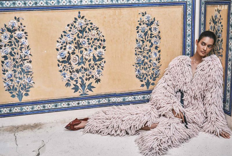 Model in textured fringe coat leaning against ornate floral painted wall for Harper's Bazaar Arabia