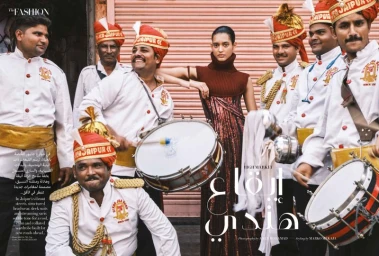 Model in a brown sleeveless turtleneck top posing amid a brass band in uniform on a street for Harper's Bazaar Arabia