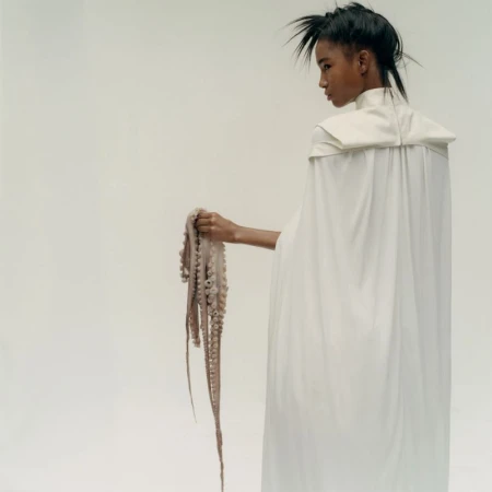 Model in long white cape holding an octopus against a plain white studio background