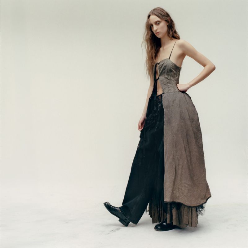 Model wearing a layered brown dress and black trousers against a neutral background