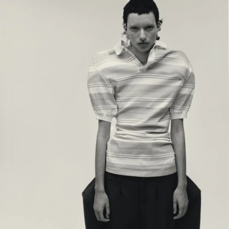 Model wearing a striped polo shirt and dark trousers against a plain seamless studio background