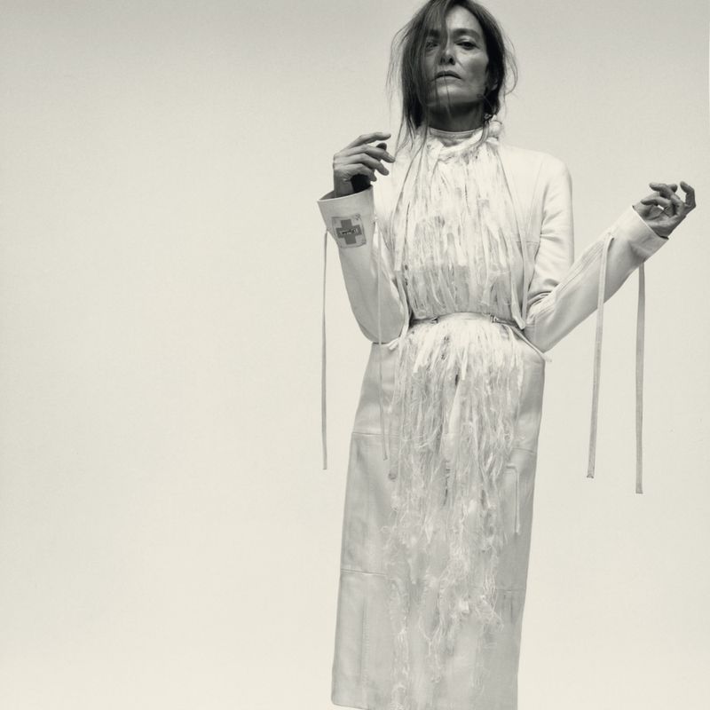 Model wearing a white fringed coat and jacket against a plain light background