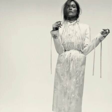 Model wearing a white fringed coat and jacket against a plain light background