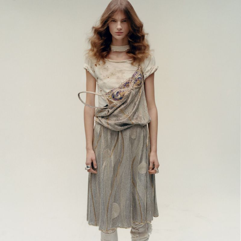 Model standing against a neutral background wearing a layered textured garment with an integrated bag detail