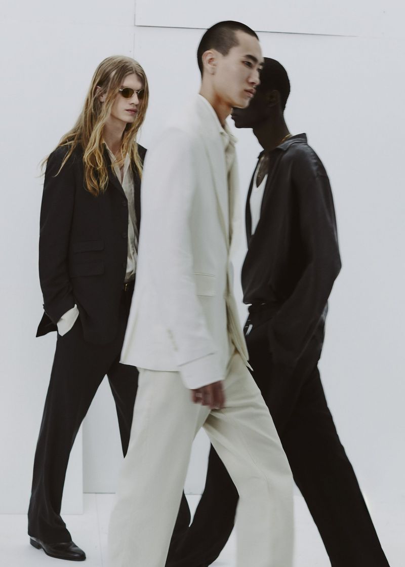 Group of four male models walking in tailored suits against a clean white studio seamless background.
