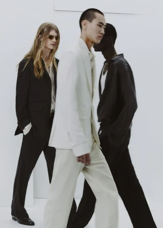 Group of four male models walking in tailored suits against a clean white studio seamless background.