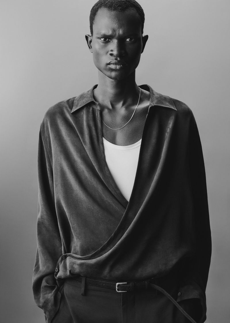 Black man wearing dark collared shirt and white tank top against grey background