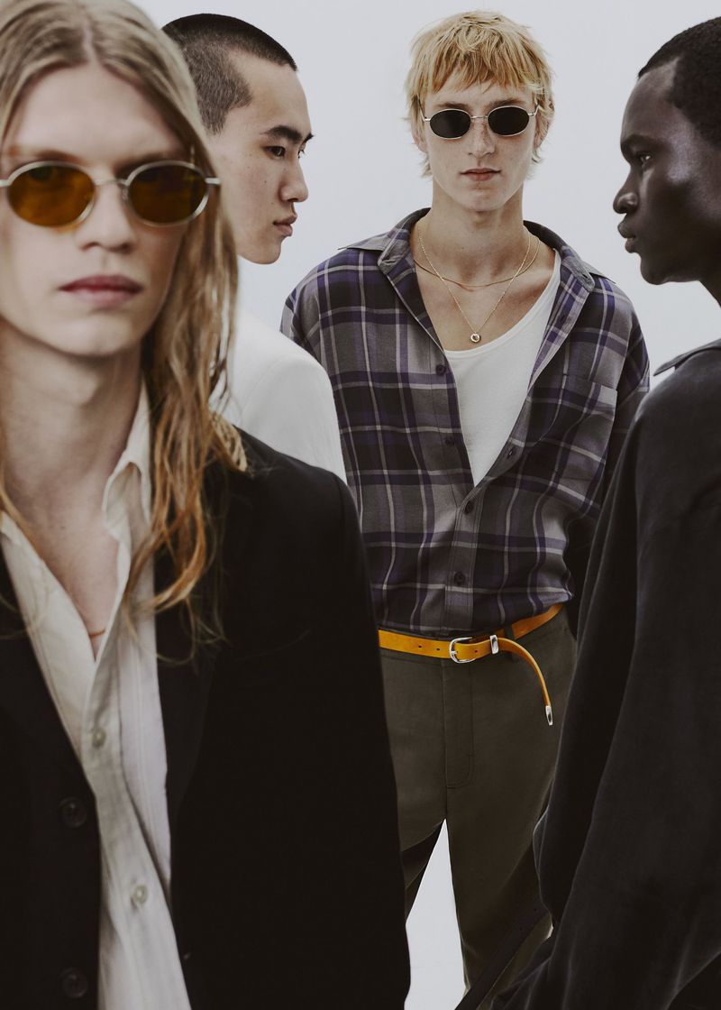 Group of four male models in casual menswear and sunglasses against a plain white studio backdrop.