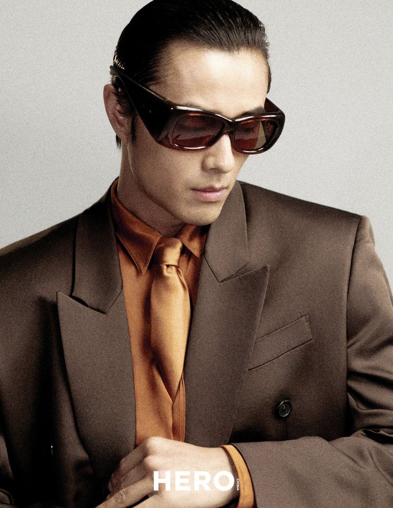 Model Zhao Lei wearing dark sunglasses, brown suit jacket, and orange shirt for Hero China by photographer Shenyun Ren.