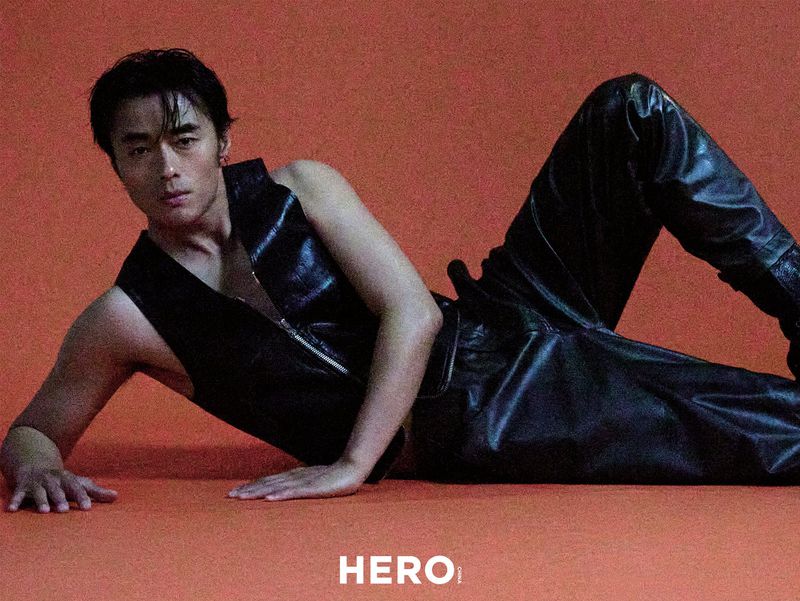 Model Zhao Lei wearing black leather vest and trousers reclining on a textured orange studio backdrop for Hero China editorial.