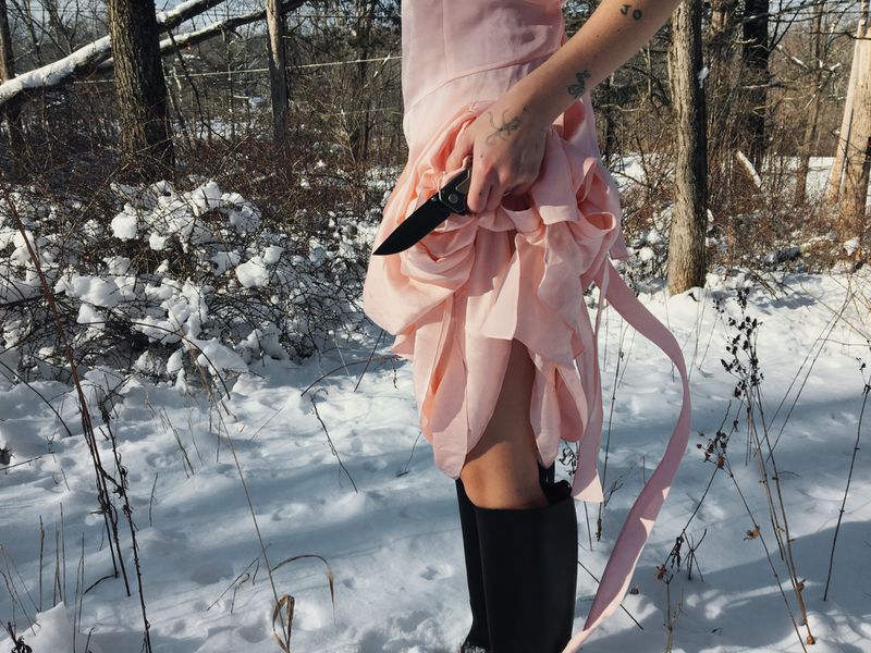 Woman in a pink dress and black boots holding a knife in a snowy forest for HommeGirls