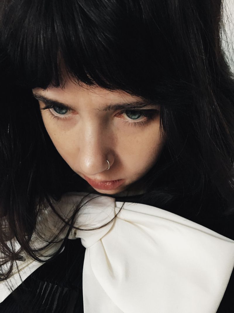 Close-up portrait of Clairo wearing a dark top with a large white bow, shot by Mitch Ryan for HommeGirls.