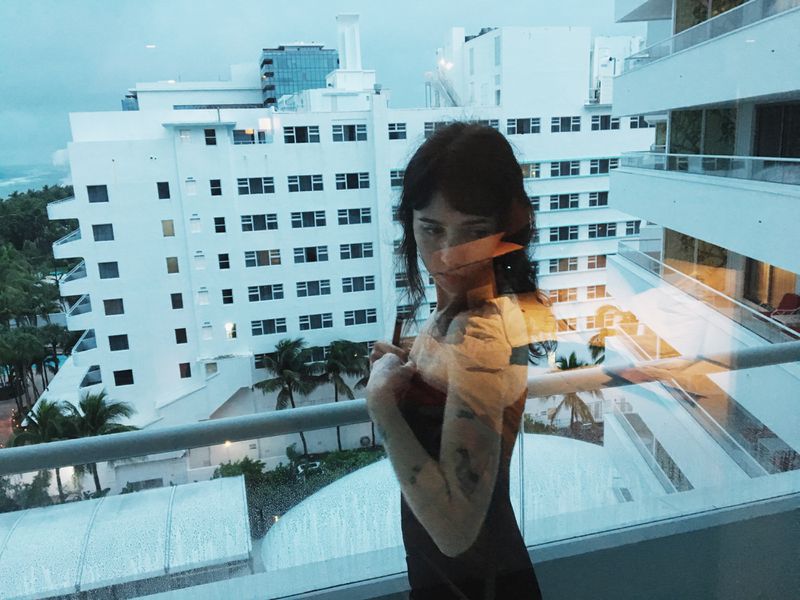 Clairo posing on a hotel balcony with white architecture in the background photographed by Mitch Ryan for HommeGirls.