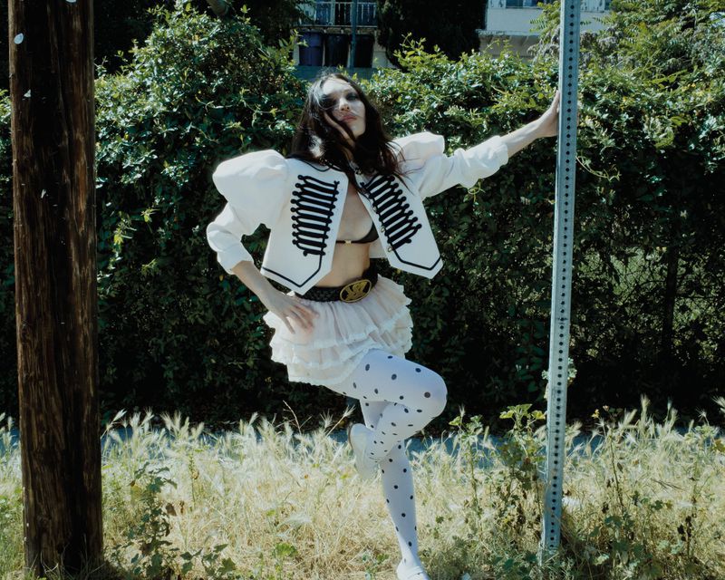 Maddie Ziegler posing outdoors wearing a white marching band jacket and polka dot tights for Rollacoaster Magazine