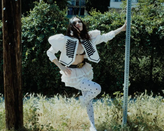 Maddie Ziegler posing outdoors wearing a white marching band jacket and polka dot tights for Rollacoaster Magazine