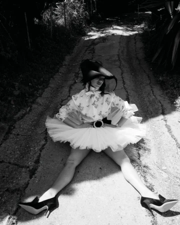 Maddie Ziegler in a white tutu and patterned blouse sitting on a rural asphalt path for Rollacoaster Magazine.