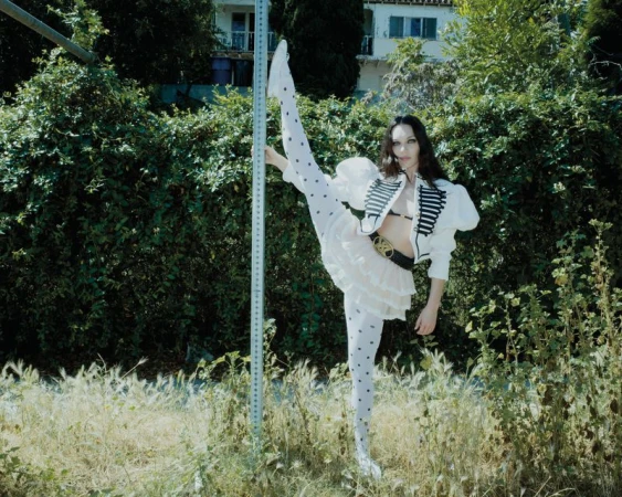Maddie Ziegler holding a metal pole outdoors, wearing white polka-dot tights and a white cropped military-style jacket for Rollacoaster Magazine