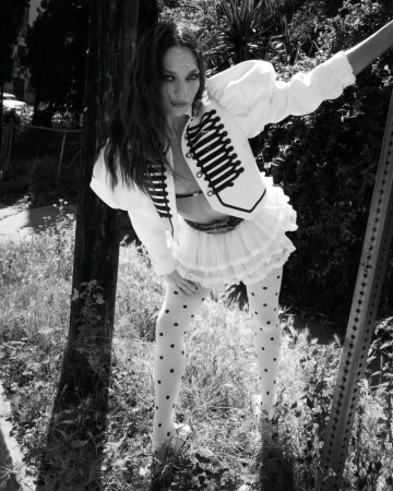 Maddie Ziegler in a white military jacket and polka dot tights leaning outdoors for Rollacoaster Magazine