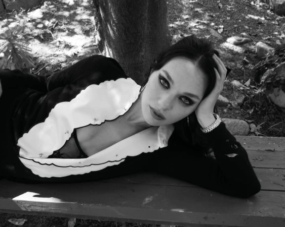 Maddie Ziegler lying on a wooden bench outdoors wearing a dark top with a white scalloped collar for Rollacoaster Magazine.