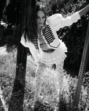 Maddie Ziegler in a white military jacket and polka dot tights leaning outdoors for Rollacoaster Magazine