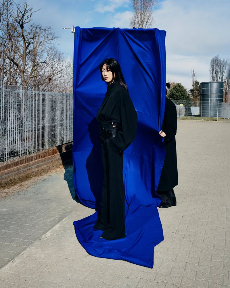 Model in black outfit posing in front of a hanging royal blue backdrop outdoors