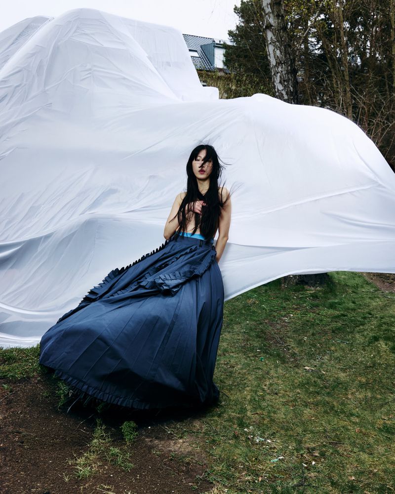 Model Loo Loo wearing a voluminous blue skirt against a billowing white draped fabric background in an outdoor setting