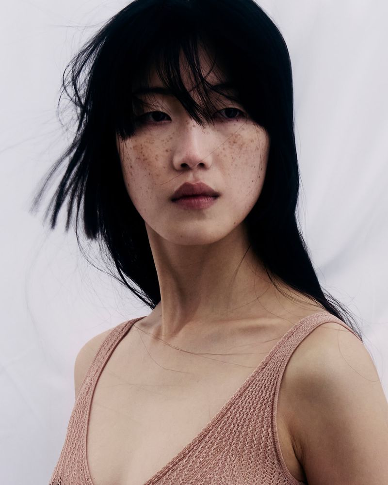 Close-up portrait of an East Asian woman with freckles wearing a patterned pink top against a white background for 10 Magazine Deutsch.