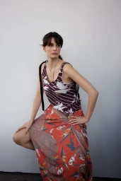 Busra Develi posing for Elle Turkiye wearing a patterned top and orange patterned skirt against a white studio wall