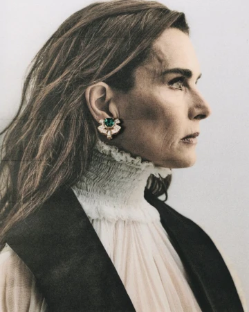 Profile portrait of Brooke Shields wearing a high-collared white blouse and ornate green gemstone earring for ODDA Magazine.