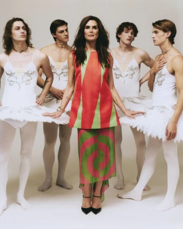 Brooke Shields standing center surrounded by four male dancers in white ballet tutus against a neutral studio backdrop