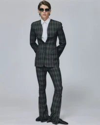 Model in dark plaid suit with flared trousers and sunglasses against a grey studio background for ODDA Magazine
