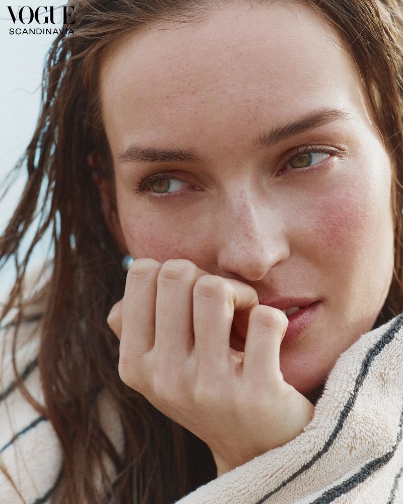 Close-up portrait of a woman with light brown hair and fair skin, featuring a white and black striped textile in the foreground.
