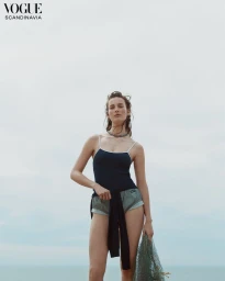 Model Julia Bergshoeff wearing a black spaghetti strap top and green shorts against an overcast sky holding a mesh net.
