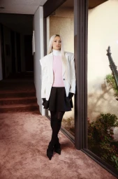 Paris Hilton standing in an indoor hallway wearing a white blazer, pink top, and black skirt for ODDA Magazine