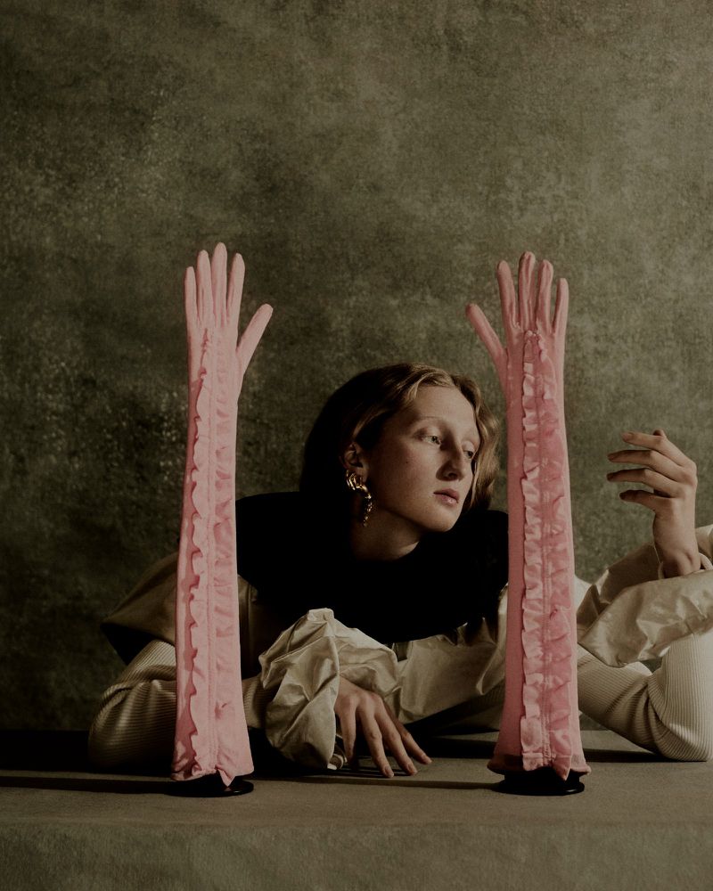 Model wearing dark clothing and pink long gloves against a mottled textured background for Telegraph Luxury