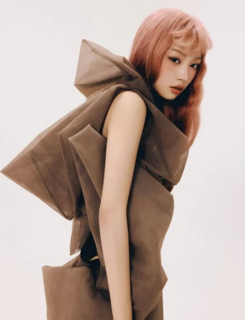 A woman with pink hair wearing a sculptural brown sheer garment against a plain white background for ODDA Magazine.